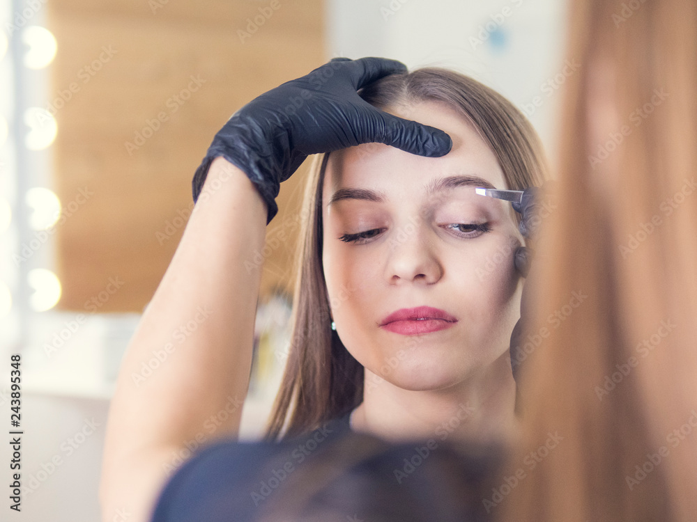 Fototapeta premium Master makeup corrects, and gives shape to pull out with forceps previously painted with henna eyebrows in a beauty salon. Professional care for face.