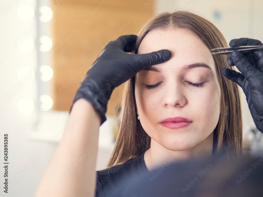 Fototapeta premium Master makeup corrects, and gives shape to pull out with forceps previously painted with henna eyebrows in a beauty salon. Professional care for face.