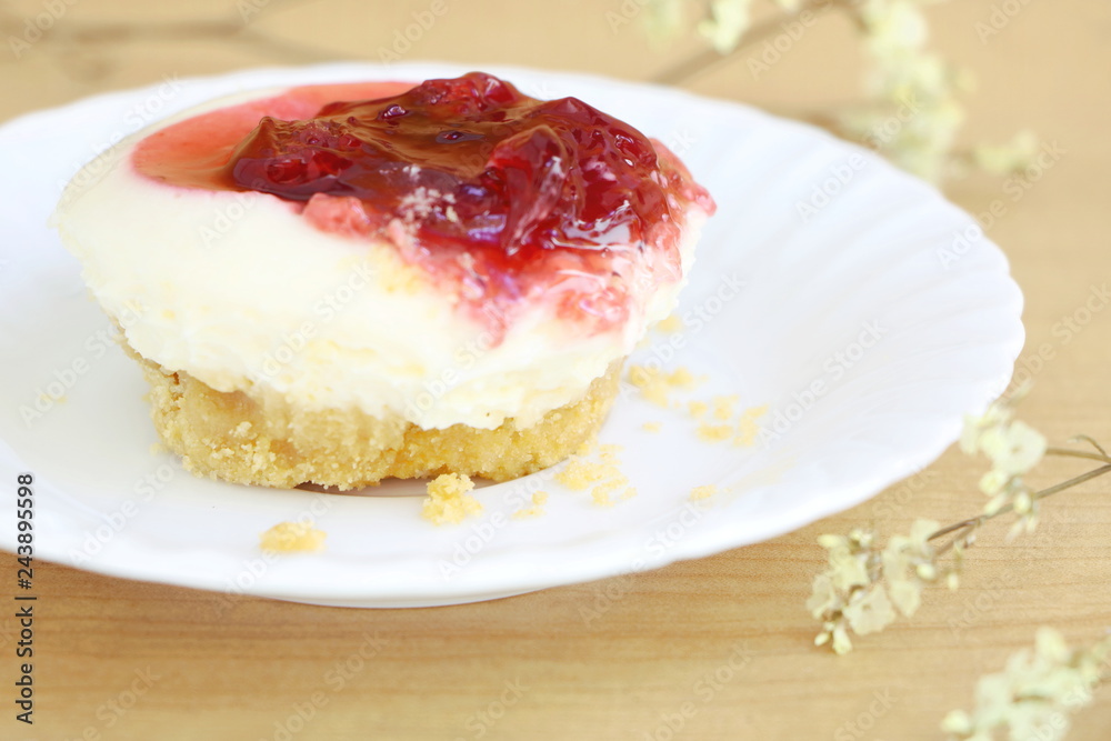 close up one piece of strawberry cheesecake with red strawberry sauce , side view on wooden table background with little white flower
