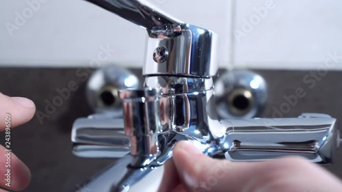 Plumber installing a mixer tap in a bathroom, he is sitting in the bathtub, close-up