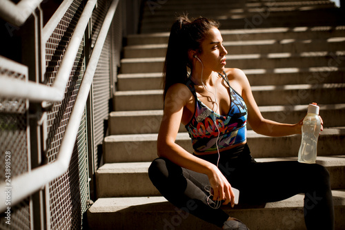 Young fit sporty woman resting and listen music on mobile phone after training outdoor on stairs in urban enviroment