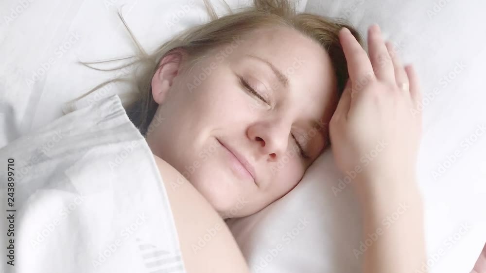 Beautiful young Woman is Sleeping on white Pillow. Girl is Waking up, Stretching and Smiling. Caucasian Female on Bed after Waking up early in Morning. Beautiful young Woman is Sleeping on white Pillow. Girl is Waking up, Stretching and Smiling. Caucasian Female on Bed after Waking up early in Morning.