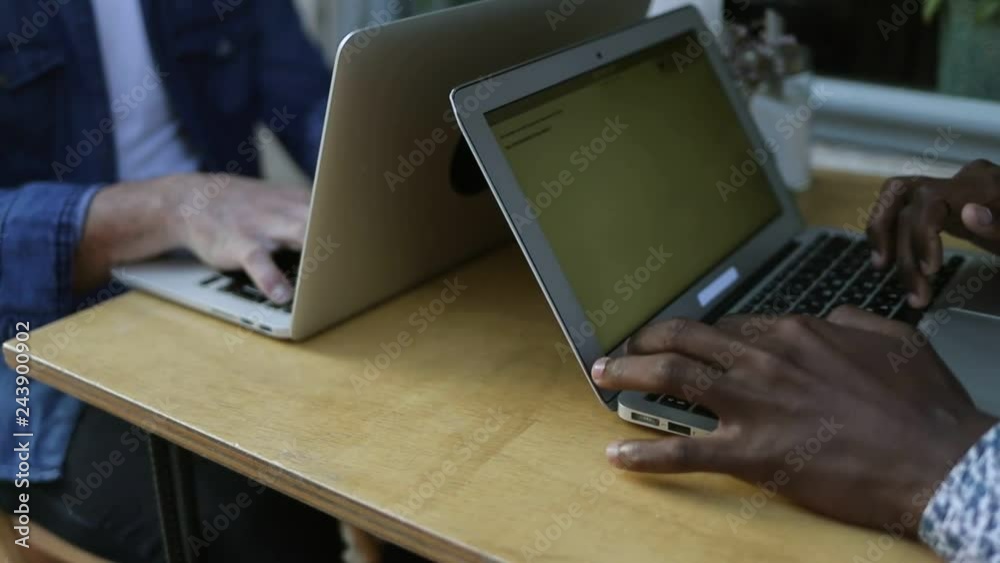 Multiethnic men working with laptops in cafe. Cropped view of young male freelancers using laptops while sitting at table in cafe. Freelance concept Multiethnic men working with laptops in cafe. Cropped view of young male freelancers using laptops while sitting at table in cafe. Freelance concept