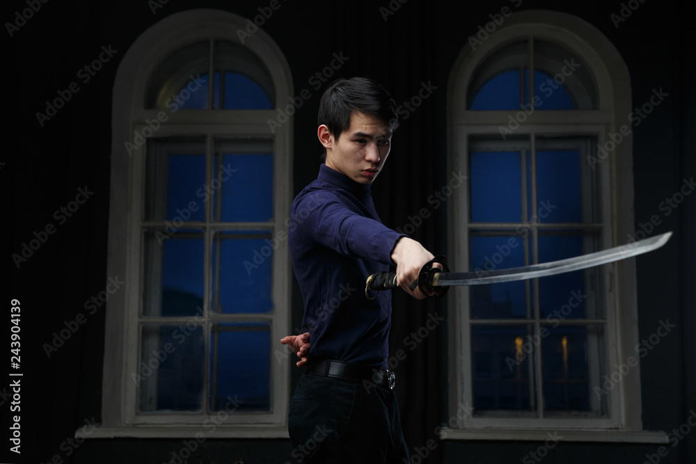 Young Asian man with a sword in his hands in a dark room.