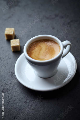 Cup of coffee and two brown sugar cubes on black stone background. Copy space.
