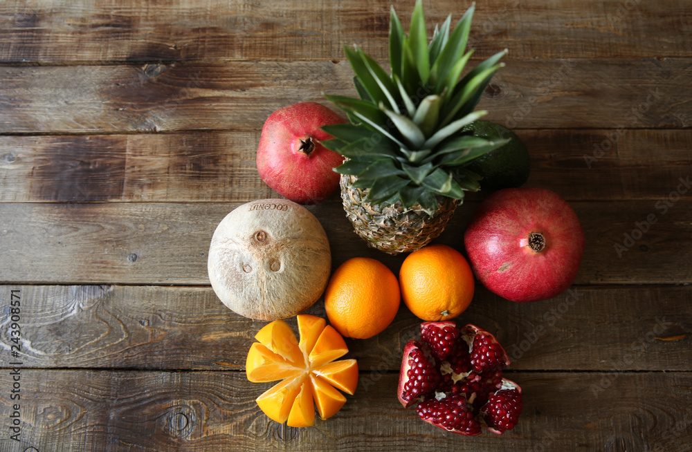 tropical fresh fruits: pineapple, oranges, pomegranate, avocado and coconut on a wooden rustic table with space for text top view, flat lay, background. Vegetarian diet.