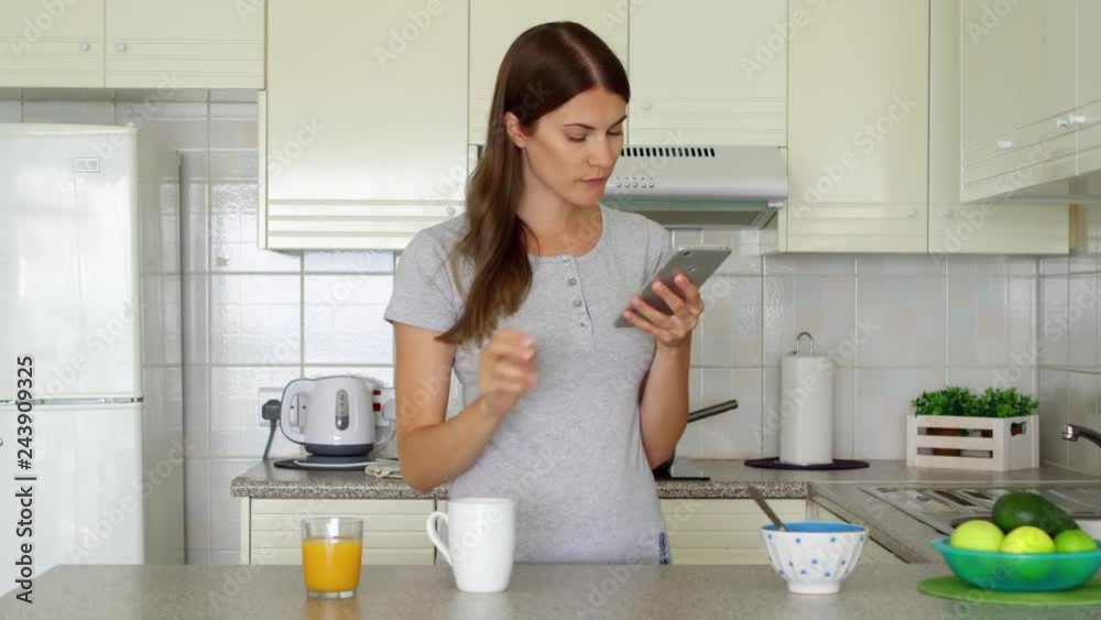 Young woman in pajamas using mobile phone. Professional female freelancer receiving good news excited happy cheerful. Female enjoying early morning standing on kitchen. Success and achievement concept Young woman in pajamas using mobile phone. Professional female freelancer receiving good news excited happy cheerful. Female enjoying early morning standing on kitchen. Success and achievement concept