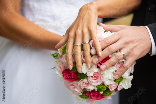 The bride and groom hold their hands with rings over a wedding bouquet with blue and white flowers