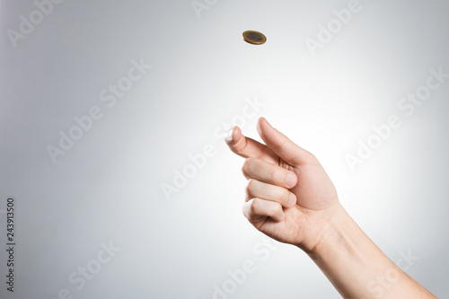 Hand throwing up a coin on gray background photo