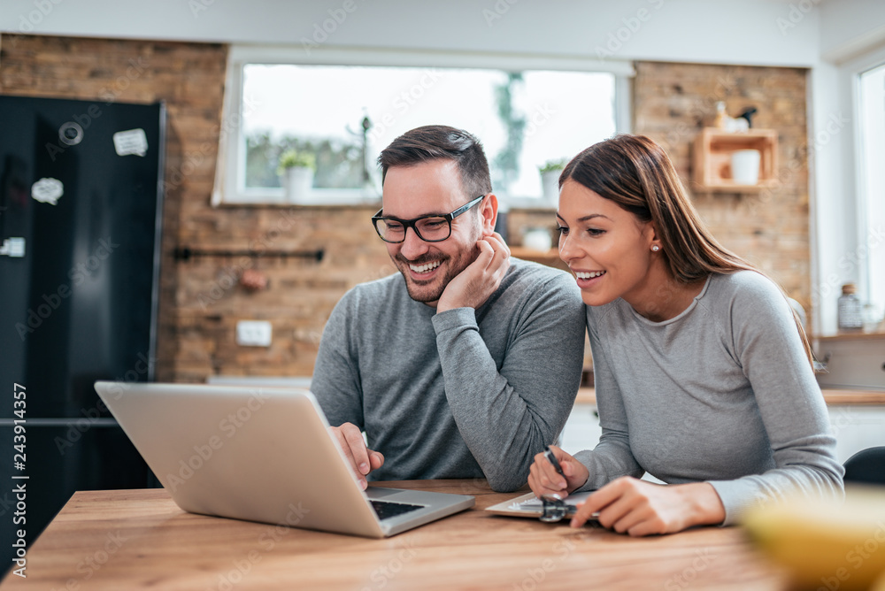 Smiling couple using laptop at the kitchen table.