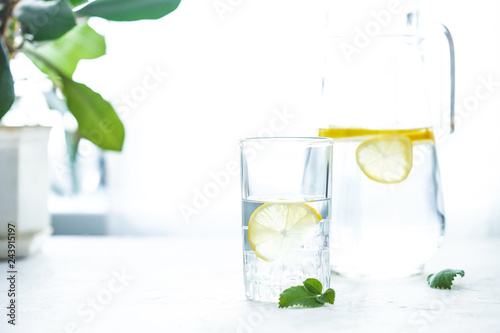 glass cup and a carafe of water, ice, mint and lemon on a white table