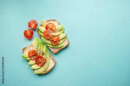 Flat lay of delicious toasts with sliced avocado, tomatoes and sesamum seeds on blue background with copyspace. Healthy food concept.