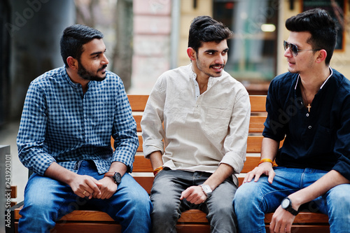 Group of three indian ethnicity friendship togetherness mans. Guys sitting on bench at street of India. photo