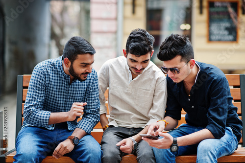 Group of three indian ethnicity friendship togetherness mans. Technology and leisure, guys with phones, sitting on bench. photo