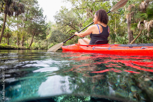Fototapeta Naklejka Na Ścianę i Meble -  Over and Under picture of a girl kayaking in a lake near an underwater cave formation. Taken in 7 Sisters Springs, Chassahowitzka River, Florida, United States of America.