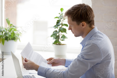 Serious businessman reading financial paper document, notification, business letter, mail, focused man doing paperwork, looking at contract, working at laptop, thinking about strategy, planning