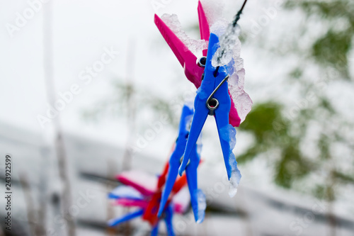 Icy colored clips for fastening laundry,frozen cord and blurred winter background.