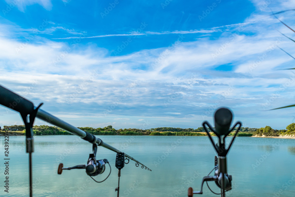 View of two fishing rods on stands with electronic lights on the background of a beautiful green lake.