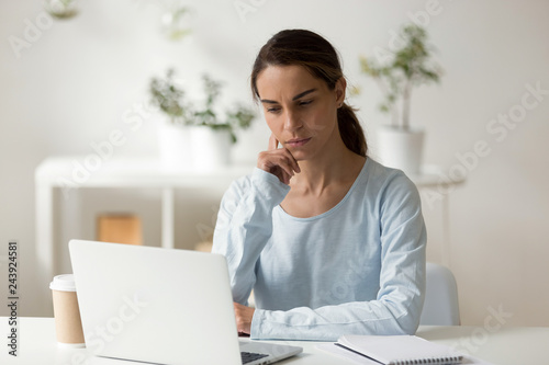 Serious female student, businesswoman, freelancer using laptop, busy, working on difficult project, looking at screen, distance learning, watching educational webinar, reading business email
