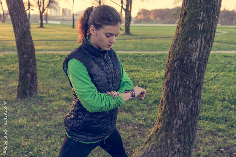 Athletic brunette cheching her progress on smart watch while exercising outdoor. Athletic brunette cheching her progress on smart watch while exercising outdoor.