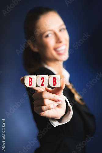 lachende Geschäftsfrau hält Würfel mit Akronym "B2B" in die Kamera