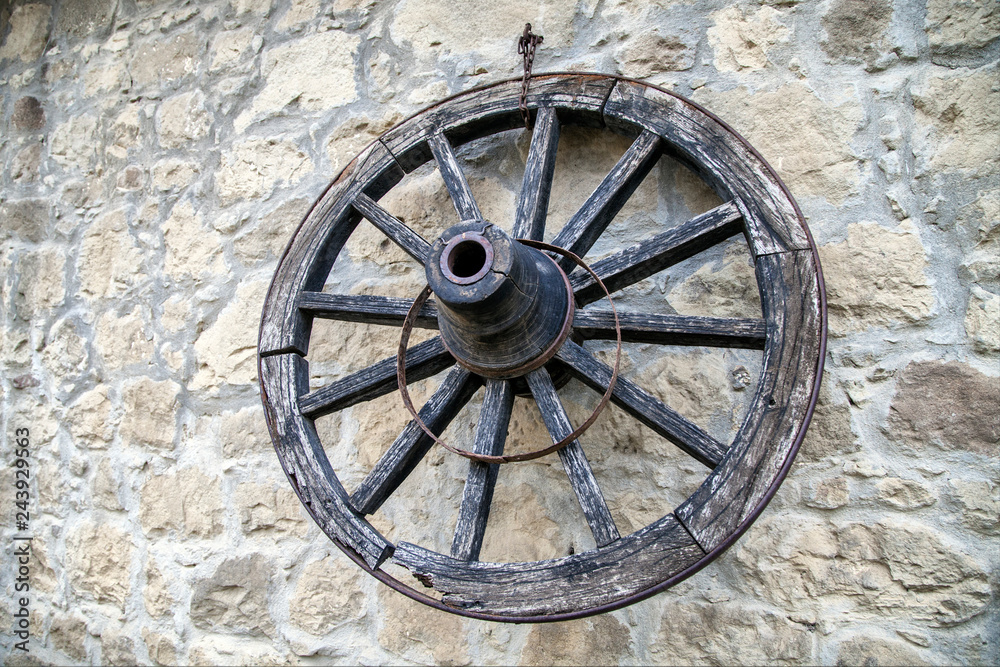Old wooden wagon wheel leaning up against a stone wall