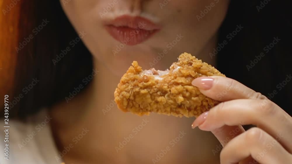 Satisfied young woman eating fatty crispy fried chicken, appetite, close up