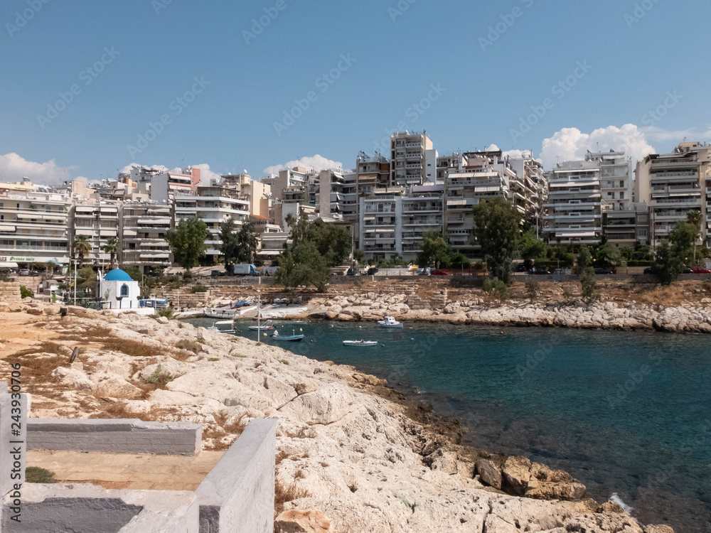 Rocky coastline of Agios Nikolaos Bay, Saronic gulf, Aegean sea, boats and Agios Nikolaos Chapel at Piraeus, Attika, Greece