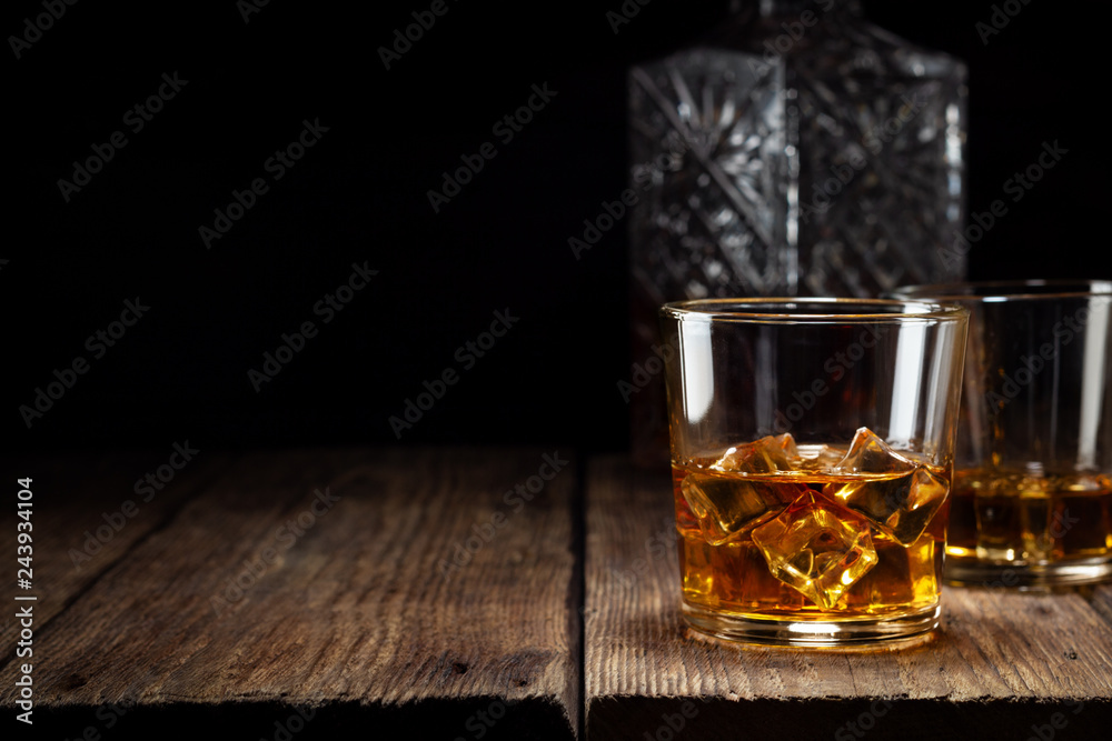 Two glass of whiskey with ice and crystal decanter on wooden table. Two glass of whiskey with ice and crystal decanter on wooden table.
