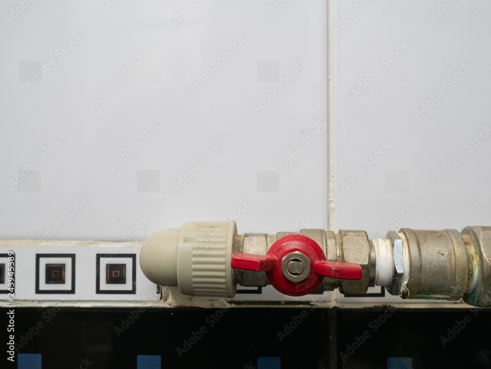 closeup of red valve which join plastic and metallic pipes in bathroom with black and white ceramic tiles