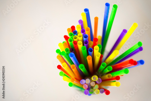 Glass full of brightly colored plastic straws sticking up next to neutral wood copy space