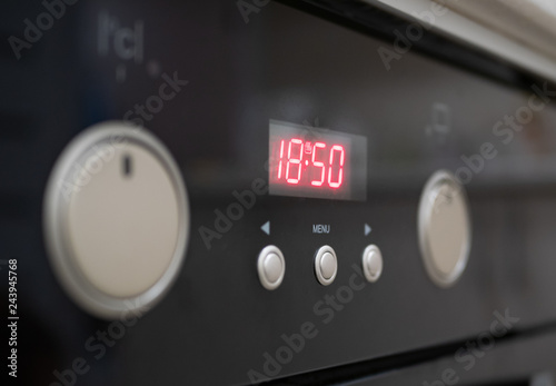 closeup of control buttons and time display of modern kitchen electrical oven. selective focus on red numbers of digital clock. control dials hidden