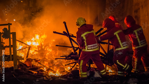 Firemen at work in uniform in from of the fire putting the rests of a burning falla sculpture made of paper at Las Fallas festival in Cullera, Valencia, Spain.