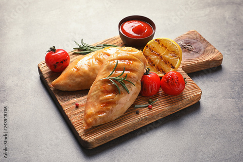 Wooden board with tasty grilled chicken breasts and garnish on table