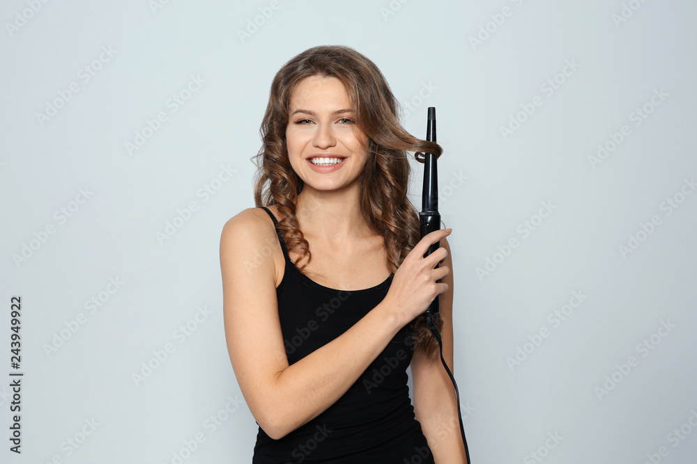 Portrait of young woman with shiny wavy hair using curling iron on color background Portrait of young woman with shiny wavy hair using curling iron on color background