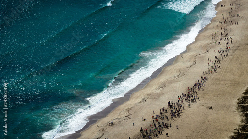 Hundreds of people running on the sand next to the waves of the Pacific Ocean. Aerial view of a marathon across the beach. From the top of Mount Maunganui Tauranga, Bay of Plenty. New Zealand.