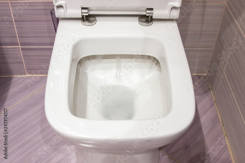 Flush in the toilet. Clean white toilet flushes water, closeup photo.