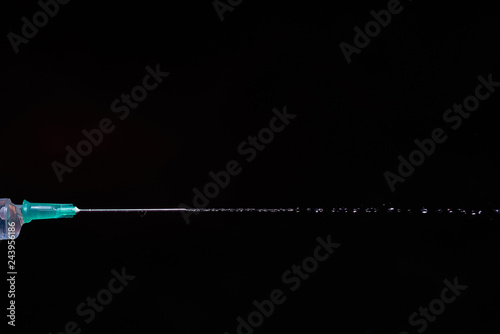 syringe on a dark background. a drop on the tip of the needle
