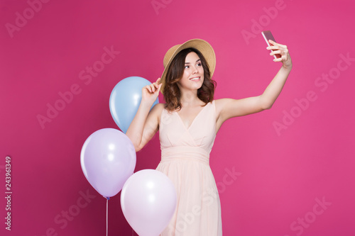 girl in a dress and straw hat makes a selfie on the background of a pink background