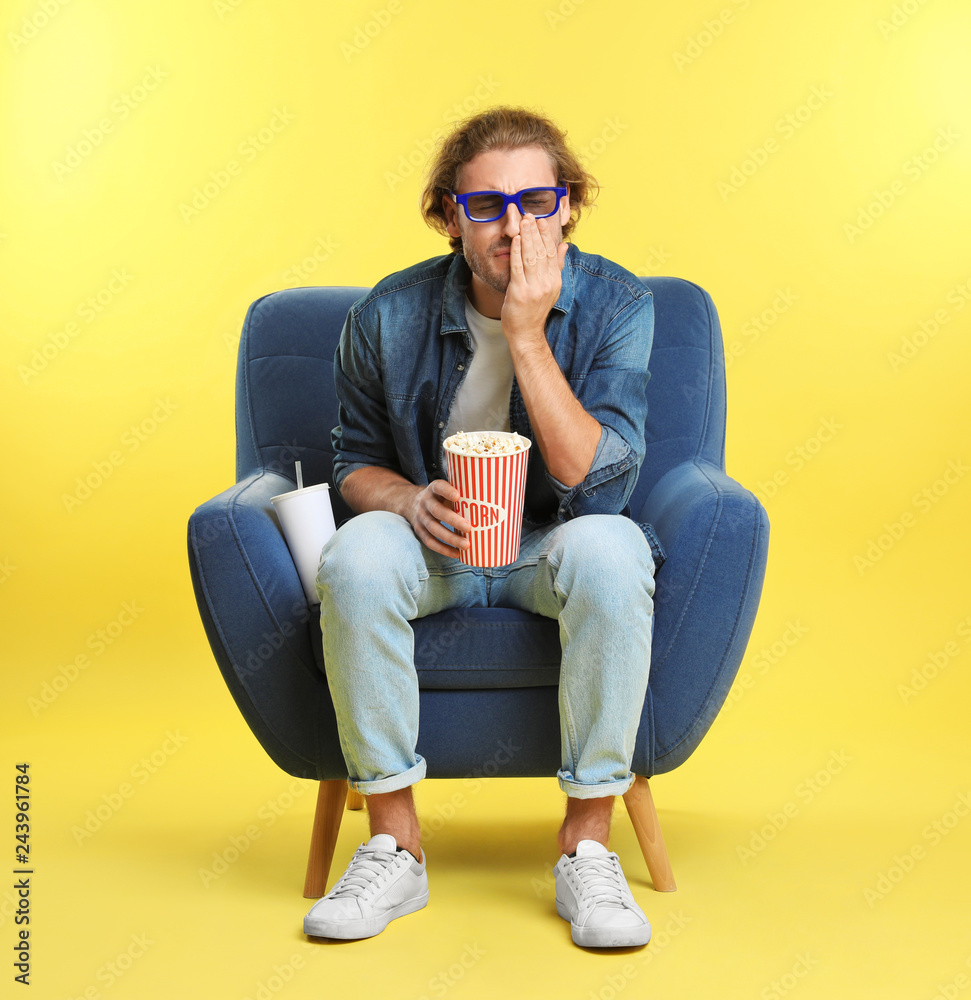 Fototapeta premium Emotional man with 3D glasses, popcorn and beverage sitting in armchair during cinema show on color background