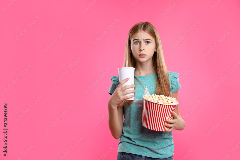 Fototapeta premium Emotional teenage girl with popcorn and beverage during cinema show on color background