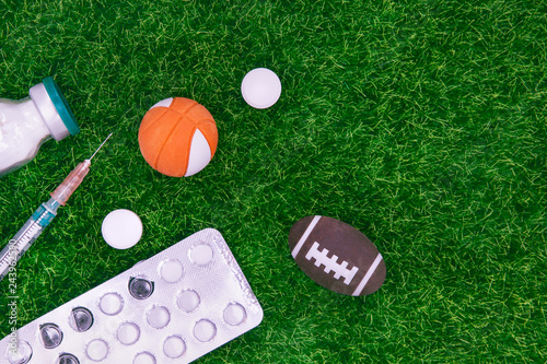 Medicines, Tablets In Blister, Syringe And Powder For Injection On Background Of Football Or Rugby Ball And Basketball Ball On Blurred Green Grass. Concept Of Doping In American Sports. Copy Space.
