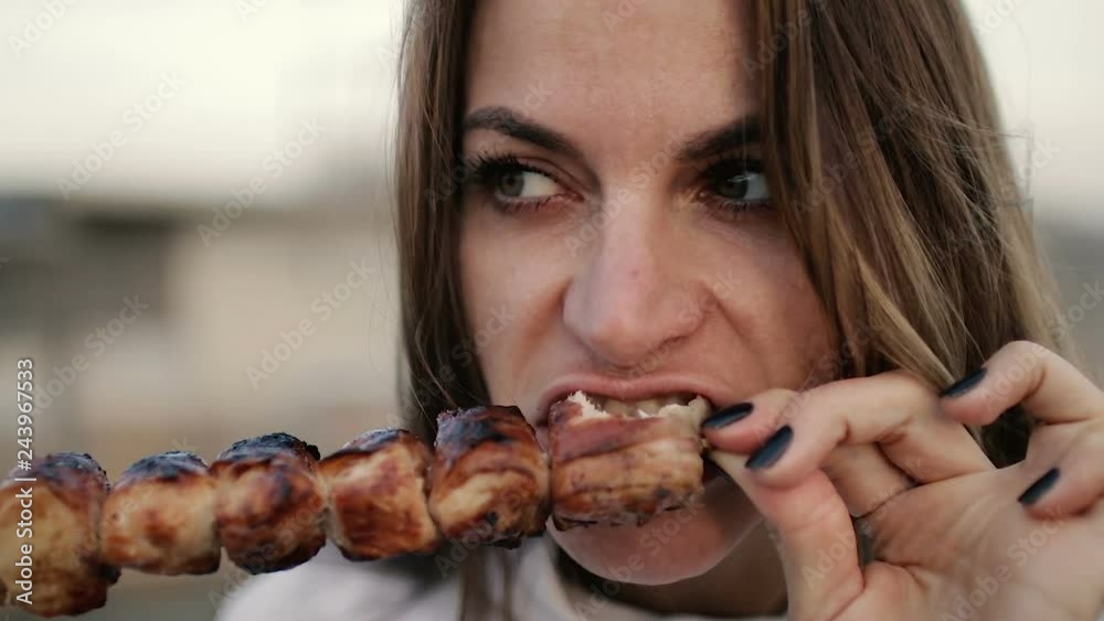 Beautiful woman biting huge pieces of meat eating with hands angry inappropriate in close up view