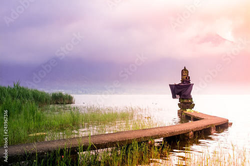 Small Hindu Temple on The Lake Side With Connecting Bridge During Sunrise in Bali on Cloudy and Misty Day with Mountain as Background photo