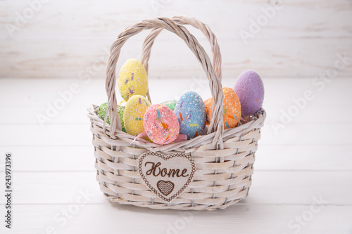 Easter eggs in a white basket on a white wooden background