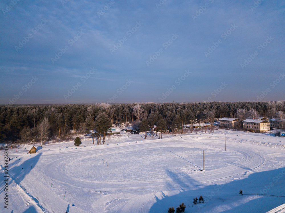 Helicopter drone shot. Aerial photography of green forest  and stadium with road, house in cold winter day.