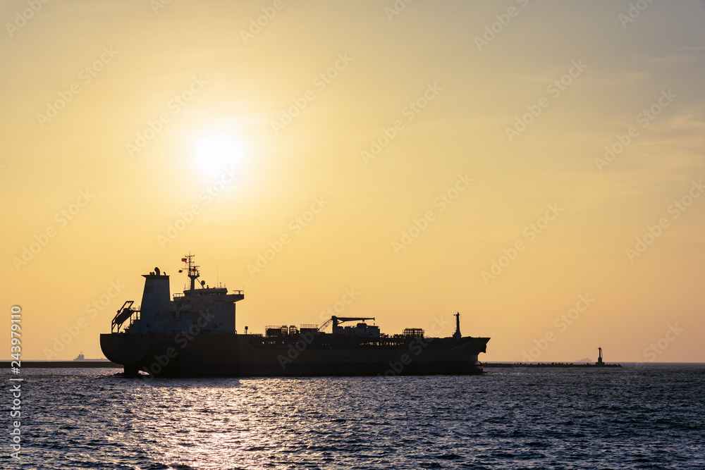 Large cargo ship leaving port as sun sets through smoggy air