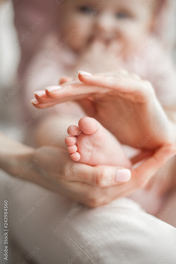 Closeup picture of baby`s little foot. Child at background with her young mother. Tiny infant`s feet at front.