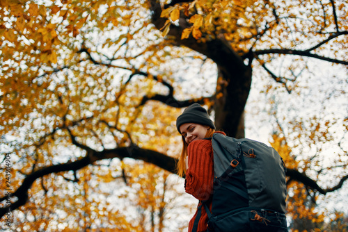 woman in a hat with a backpack standing near yellow tree autumn forest