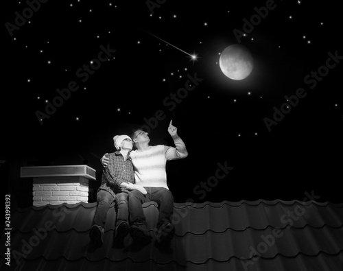 A married couple is sitting on the roof of a house at night.